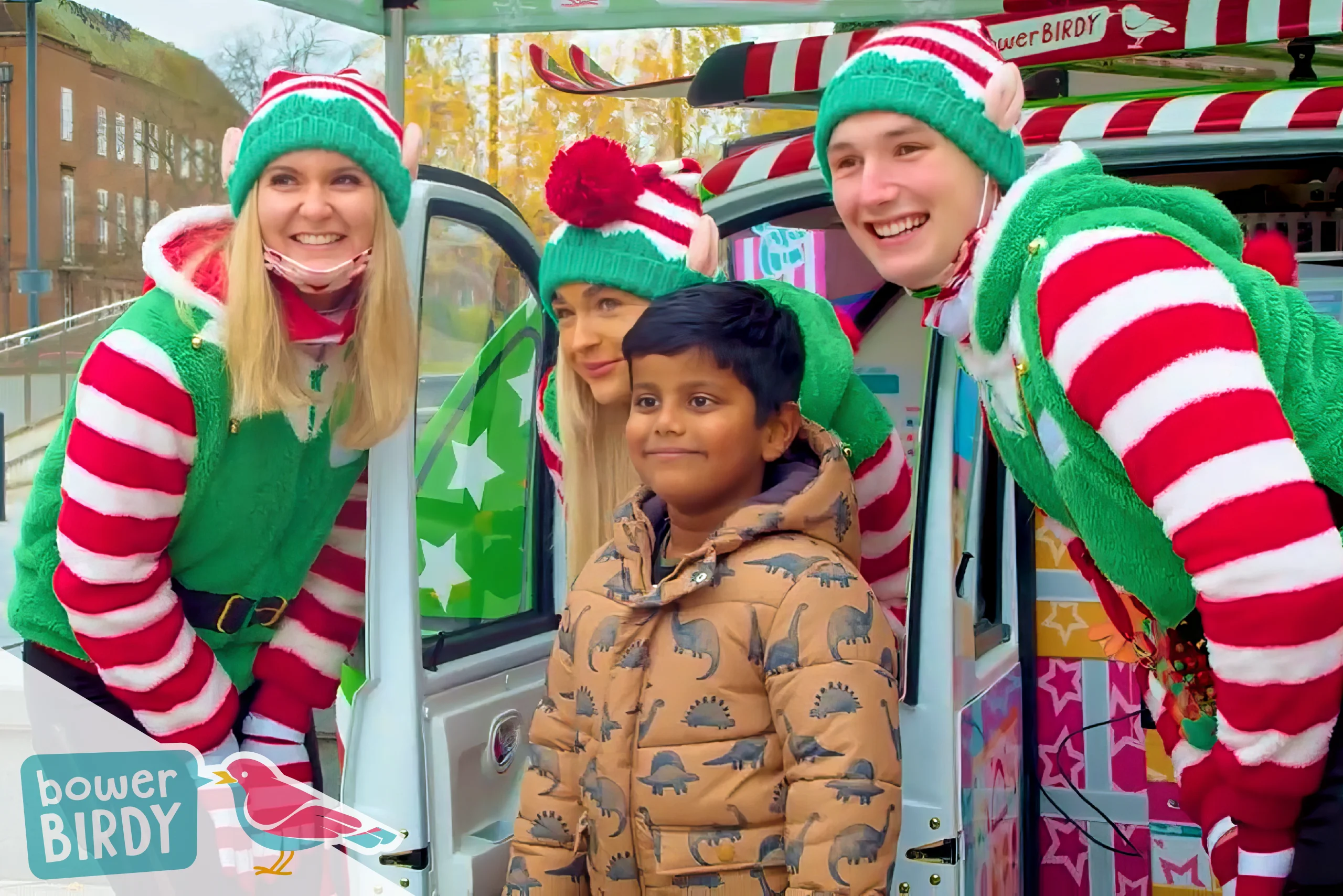 Three Bowerbirdy elves smile with a young boy, in front of the Elf Car