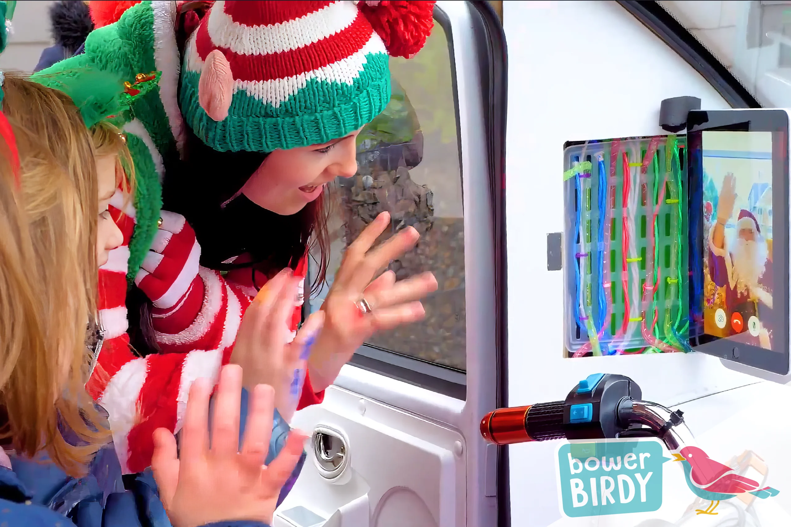 Christmas in Streatham - Two young girls sitting in the front of Bowerbirdy's Magical Elf Car, waving to Santa video video call on an ipad mounted inside, along with a Bowerbirdy elf.