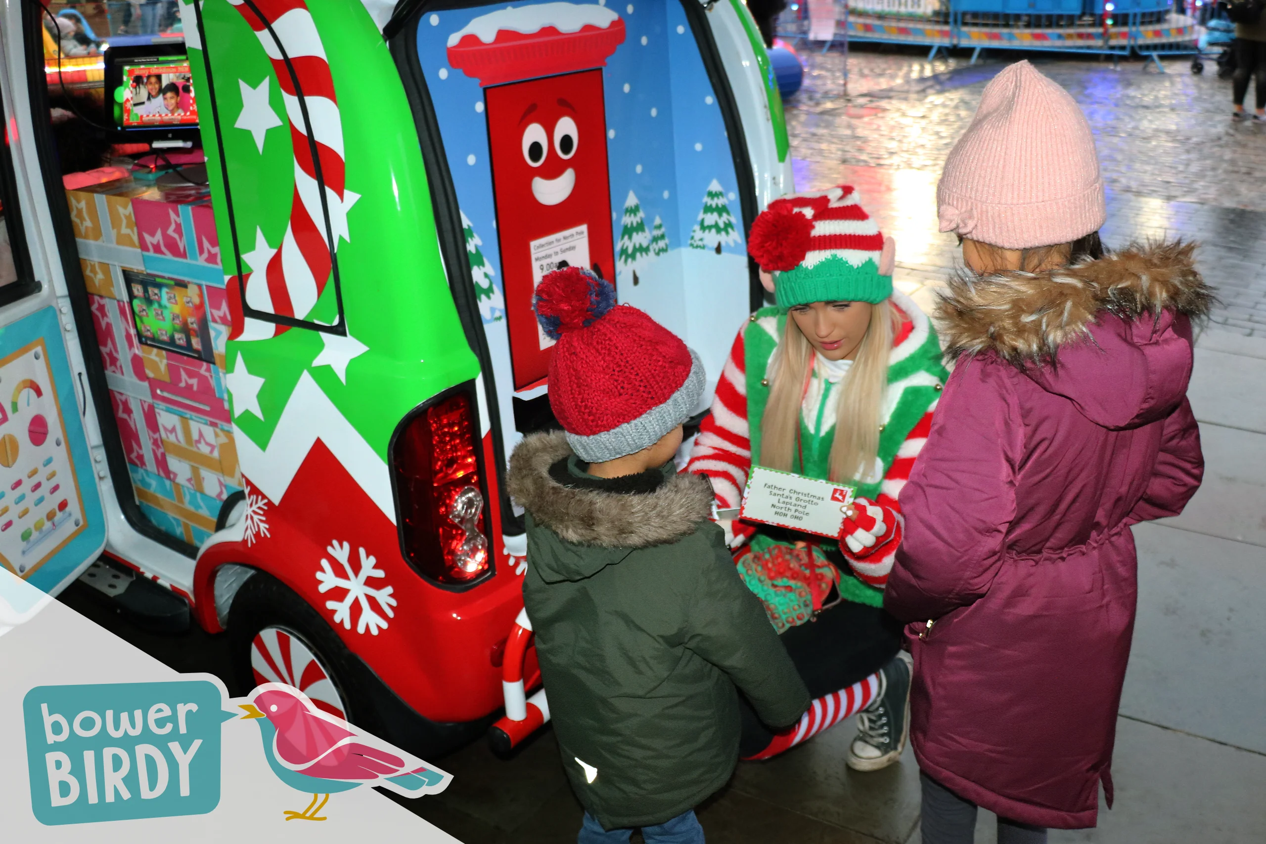 Elf Car Christmas Event: A Bowerbirdy elf helps two young children to write their christmas lists in front of the Enchanted Postbox.
