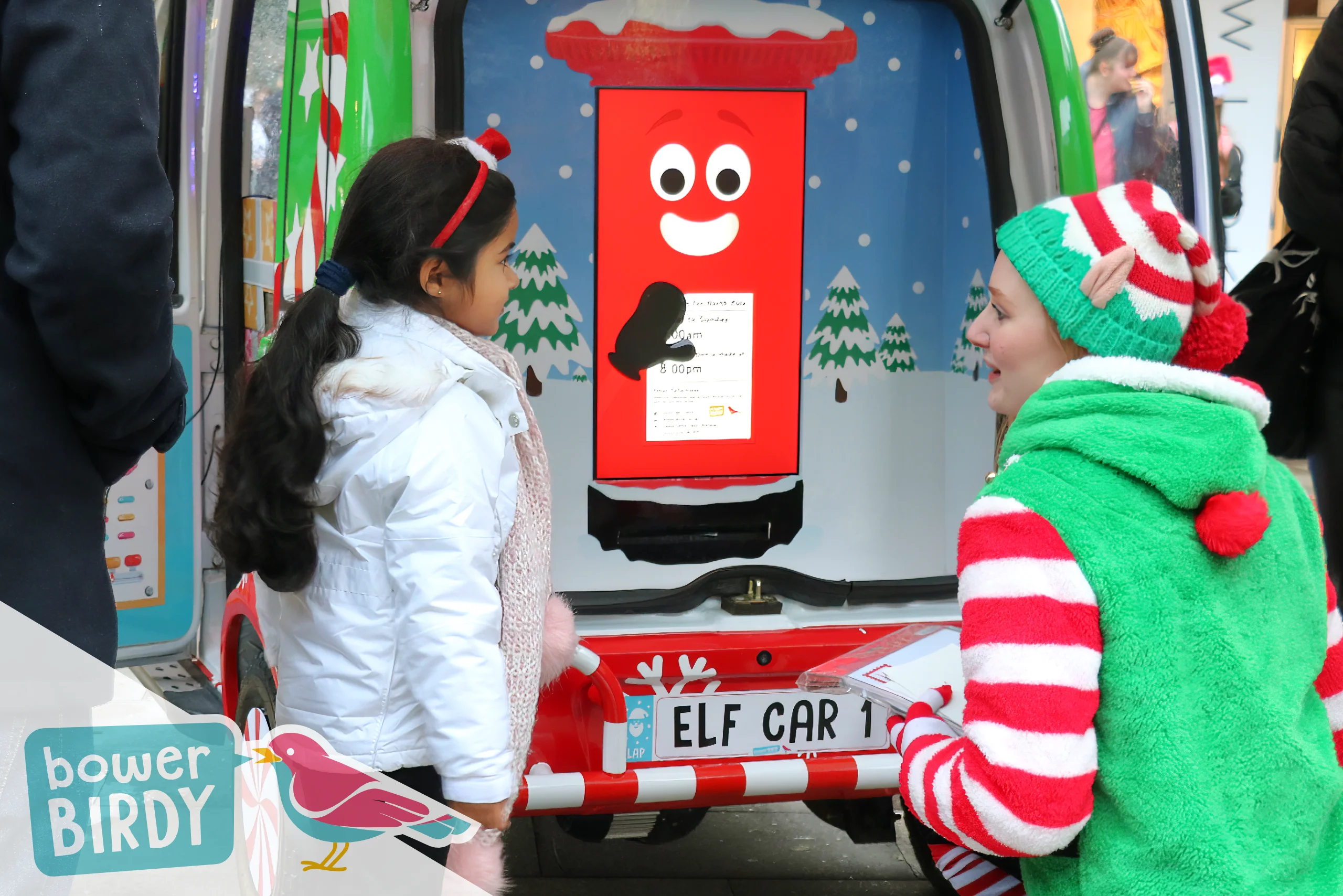 Elf Car Christmas Magic in Stevenage: The Enchanted Postbox waves between a girl and a Bowerbirdy elf.