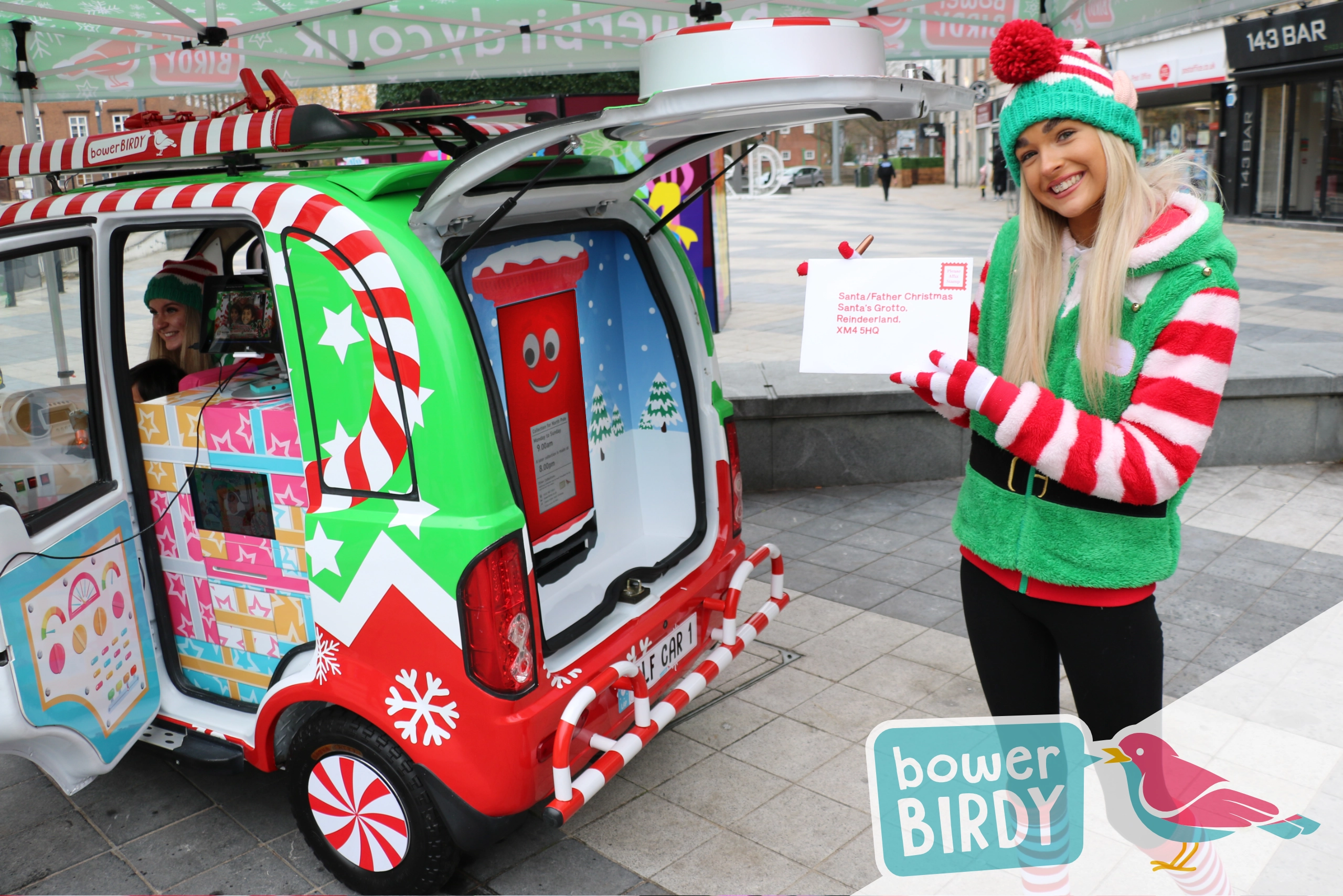 A Bowerbirdy elf holds up a letter to Santa next to the Elf Car