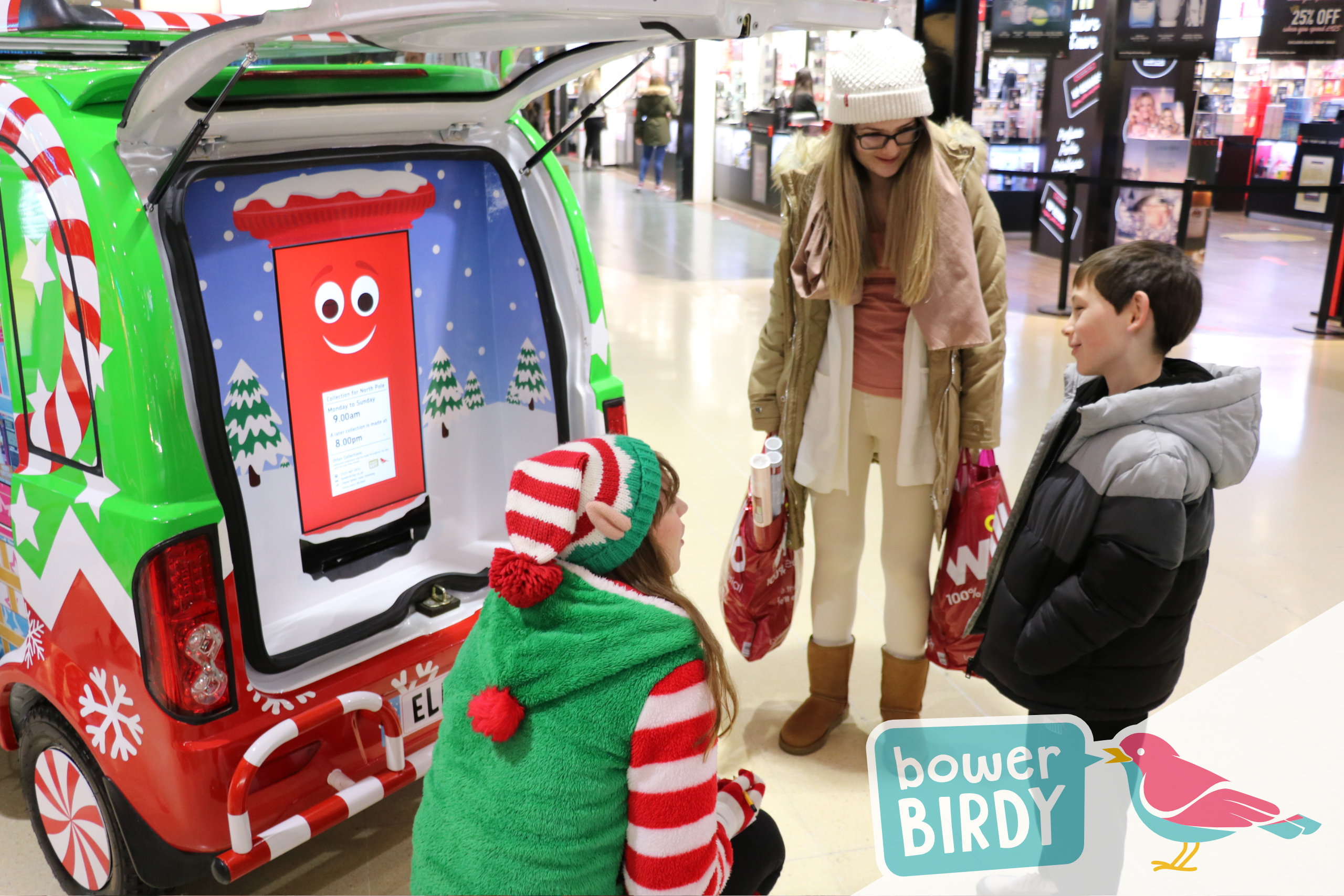 A boy talks to a Bowerbirdy elf as his mum looks on