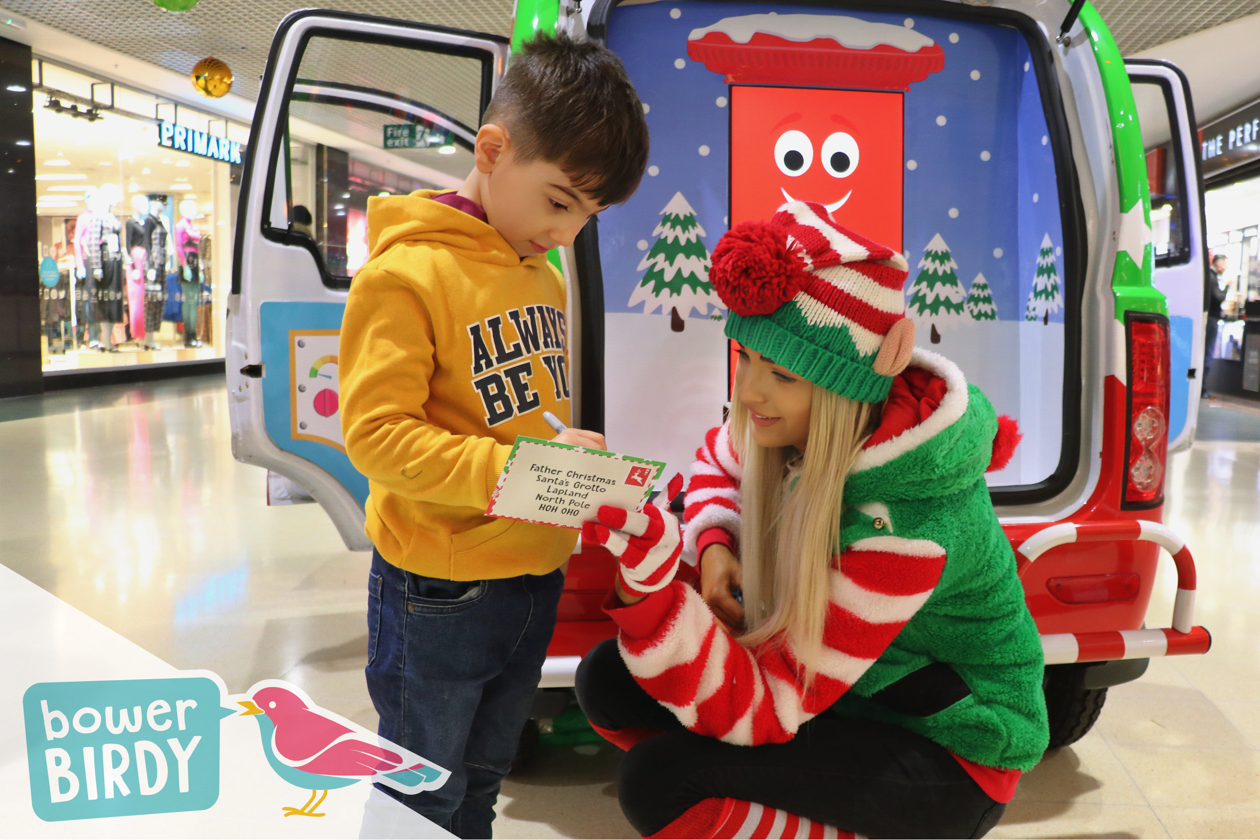 Christmas Shopping Centre Events: A boy writes his Christmas list with the help of a Bowerbirdy elf.