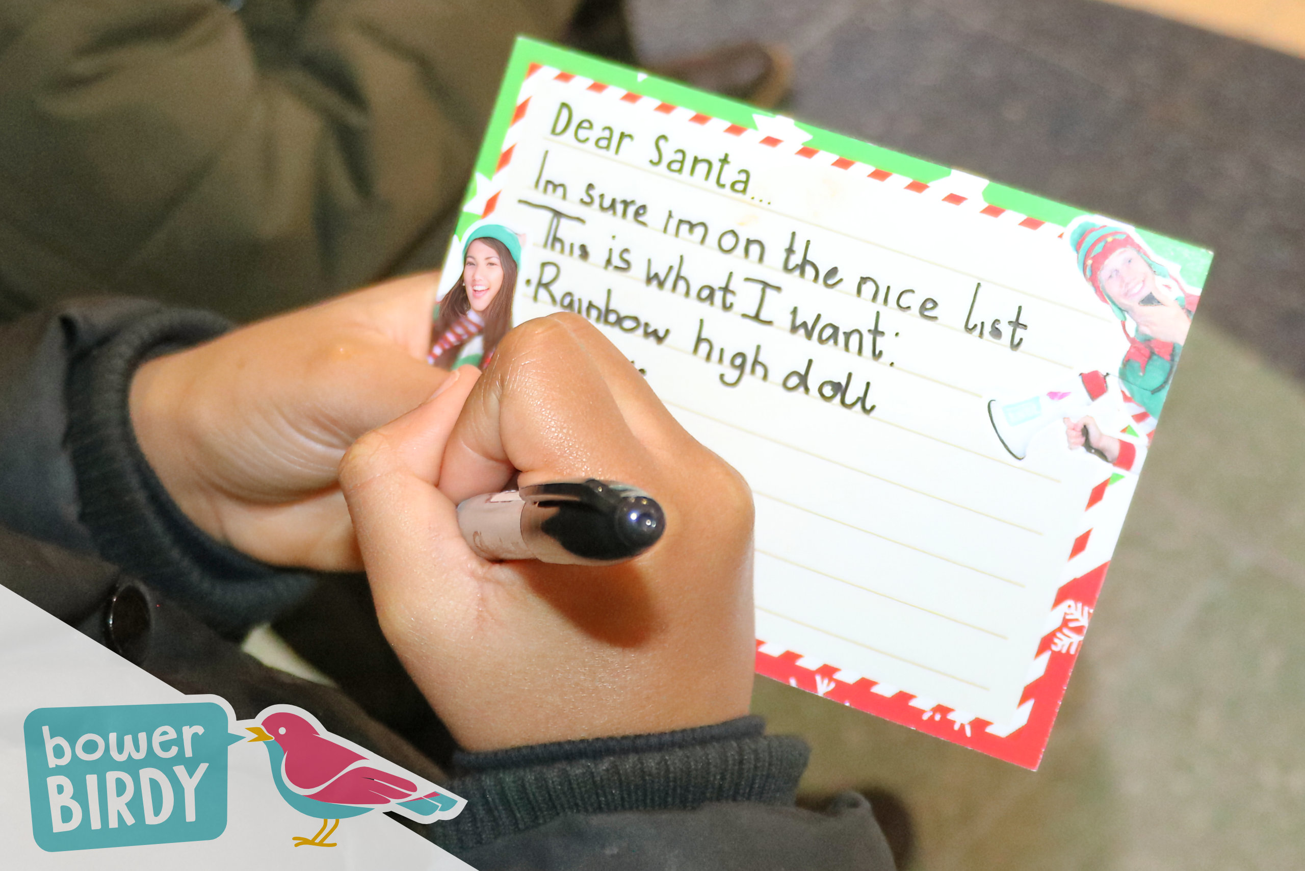 A close up of a child's hands writing their Christmas list on a Bowerbirdy Elf Car postcard.